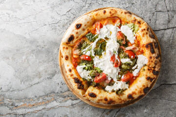 Delicious authentic pizza with stracciatella cheese, pesto, ham and cherry tomatoes close-up on a...