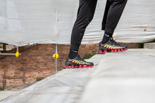 A side view of a person wearing black Nike Shox sneakers with a vibrant red and yellow gradient, walking up stone stairs. Rome, Italy - March, 2026