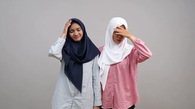 Two confused Asian women wearing hijab are doing face-palm gesture