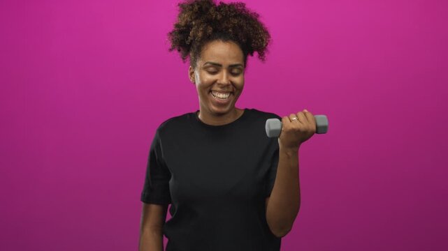 Woman curling a dumbbell with bare forearm visible, smirking while exercising in a magenta studio; confidence.