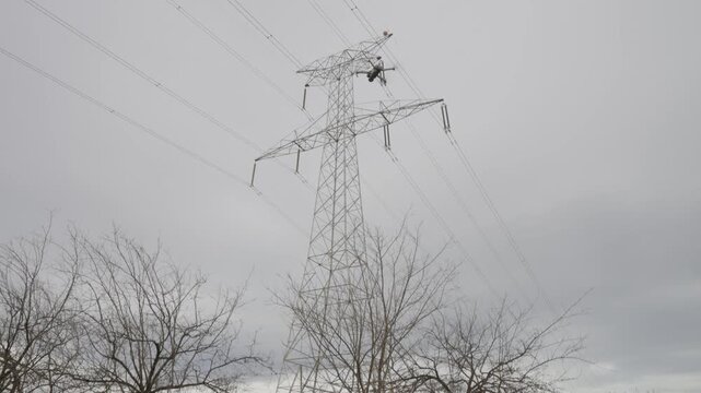 A male engineer operating a drone to inspect a high-voltage power line pylon. A professional using new technology for grid maintenance