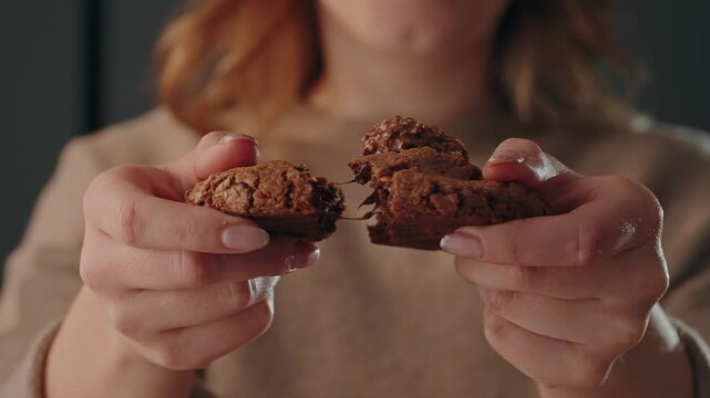 Close up hands pulling apart chocolate cookie showing gooey center indoors