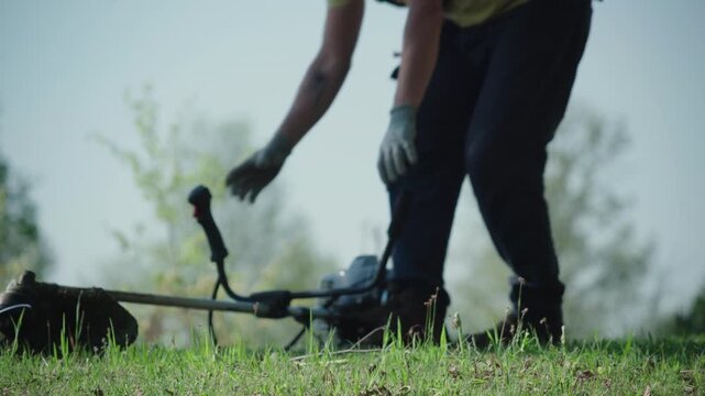 Out of Focus Gardener Man Starts Brush Cutter, Grass Foreground STATIC