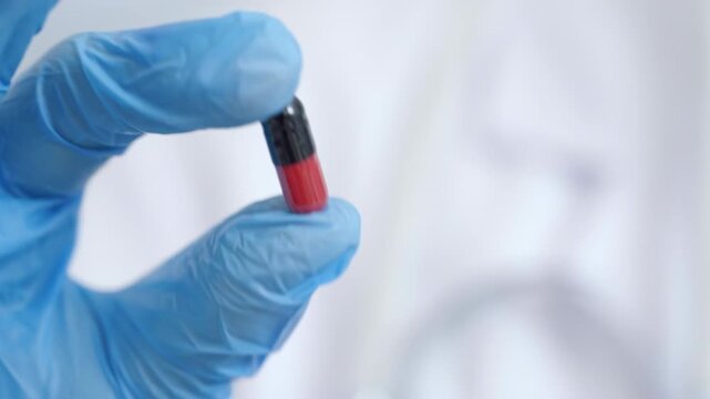 Close up of unknown woman doctor pharmacist holding red and black capsule pill medication healthcare medical lab, emphasizes the importance of pharmaceuticals in treatment and medicine