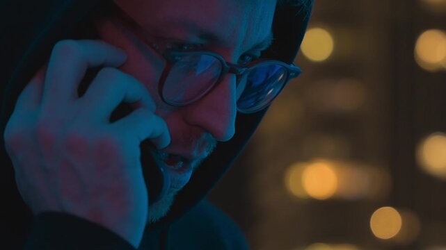 man having secretive phone conversation at night in urban location. Person making suspicious call outdoors with concerned expression. Late night communication suggesting covert activity, private talk
