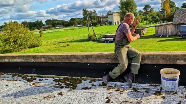 Man pulling up bucket with sand as fixing materials, sitting on the ledge of flat roof
