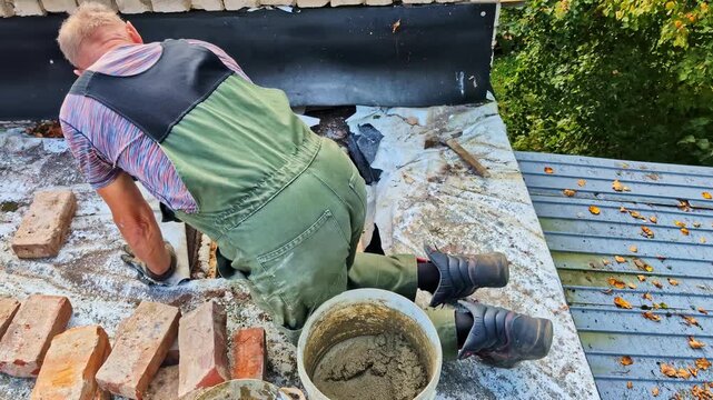 Skilled master bricklayer working on a residential roof, renovating a chimney, Man applying mortar to bricks, repairing a chimney on a household roof