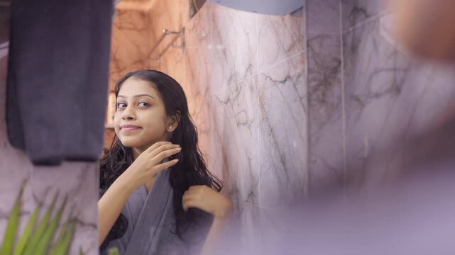 Beautiful lady admiring herself in the bathroom mirror, touching her hair gently during her morning routine.