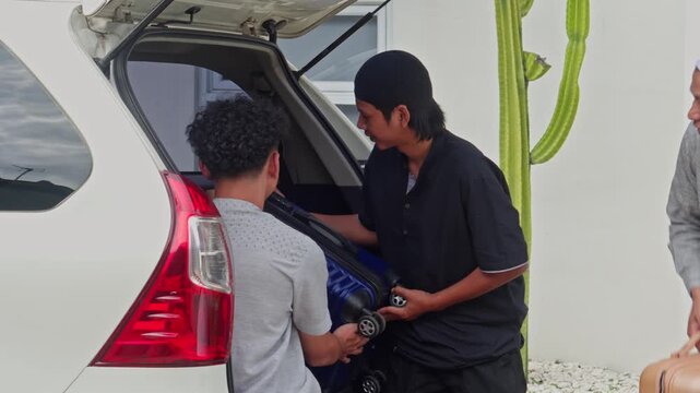 Three young Muslim men loading suitcases into car trunk for Mudik holiday travel
