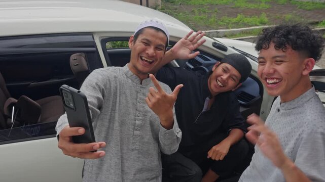 Three happy Muslim men taking a selfie and laughing by white car during Mudik