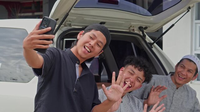 Three happy Muslim men taking selfie and laughing together while sitting during Mudik holiday trip