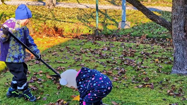 Children and adult cleaning garden, raking autumn leaves together anr picking up rotten apples