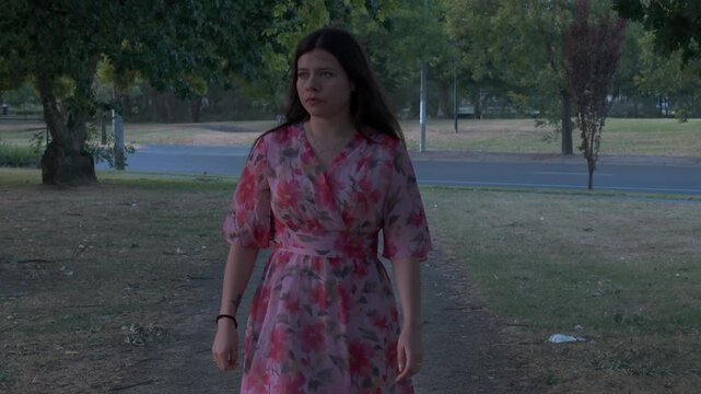 A young woman strolls through Croydon Park, Melbourne, wearing a floral dress. The peaceful setting highlights the park's greenery and tranquility, captured in a medium shot.