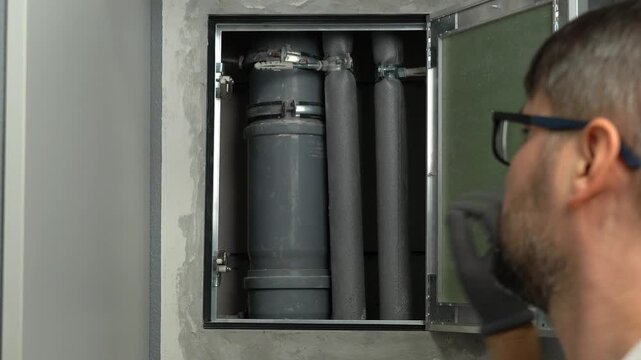 Repairman installs hidden technical inspection hatch in wall to access sewer pipes in kitchen or bathroom. Checking door opening and closing