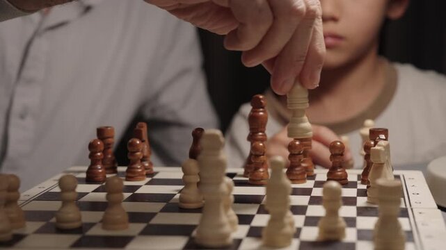 Father captures child&rsquo;s knight during chess game while boy reacts to the move. Close emotional moment showing competition, strategy and learning through play at home.