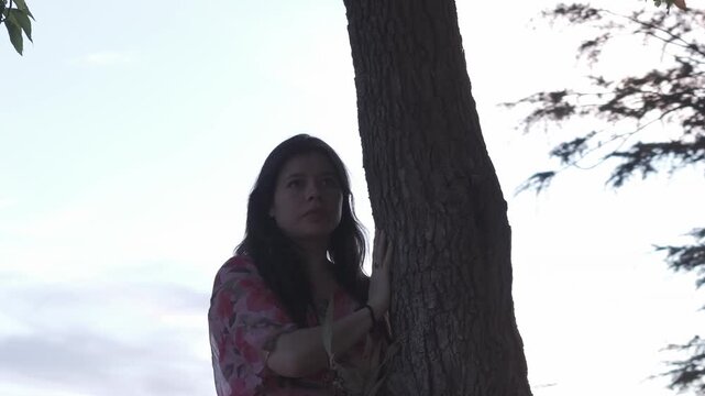 A woman stands quietly by a tree at dusk in Croydon Park, Melbourne. The serene, natural setting highlights her thoughtful expression. Soft lighting adds a tranquil feel.