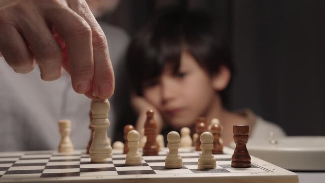 Close view of father moving chess king while son in background quickly captures a rook. Concept of strategy, counterattack, learning and competitive family play.