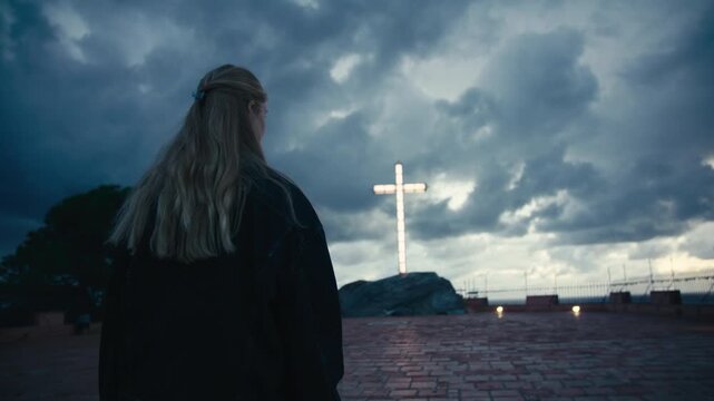 Woman standing before a glowing white cross under dark storm clouds, symbolizing faith, hope, and light in uncertain times.