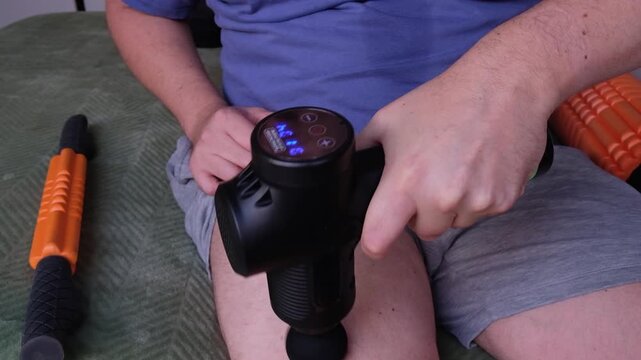 Closeup: Man uses percussion massage gun to relax tight thigh muscles