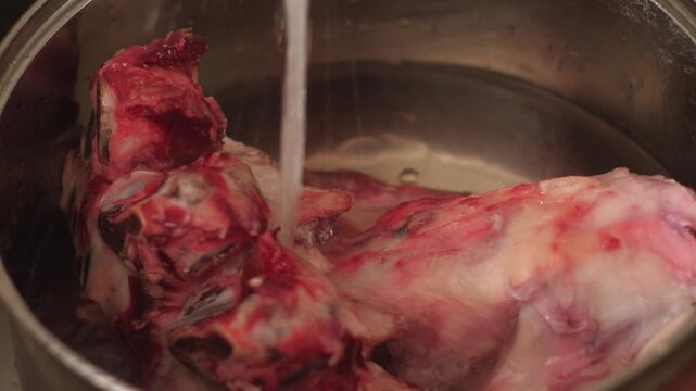 Process of pouring clean water over fresh beef bones and meat in a steel pot. Preparing natural ingredients for boiling homemade meat broth.