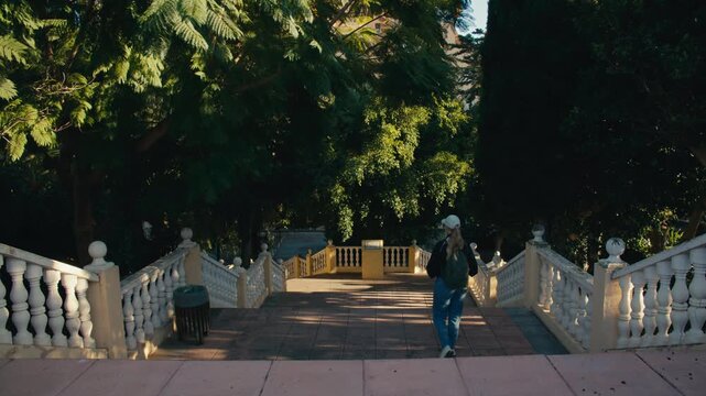 Woman descending elegant stairway surrounded by lush greenery in a tranquil park in southern Spain.