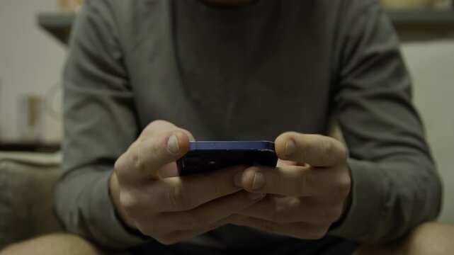 Man scrolling a smartphone, mobile phone with both hands. Person procrastinating. In home house