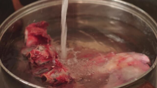 Fresh beef bones in a pot are gradually filled with cold running water. Preparing meat ingredients for long simmering of a rich homemade broth