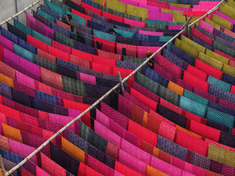 Narayanganj, Bangladesh - 08 March 2026: Aerial view of vibrant textiles drying in the sun, a kaleidoscope of reds, blues, and pinks stretching across the frame.