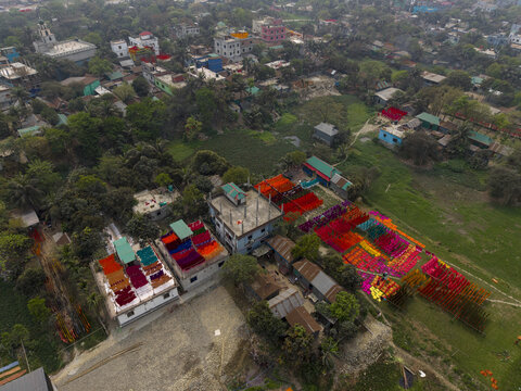 Narayanganj, Bangladesh - 08 March 2026: Aerial view of vibrant textiles drying in the sun, creating a stunning contrast against the lush greenery and urban landscape.