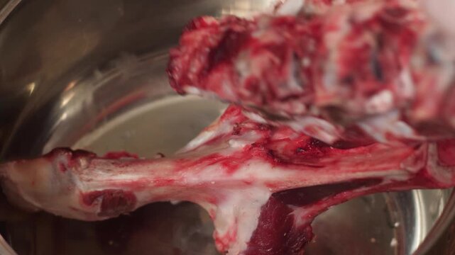 The cook puts large beef bones and pieces of raw meat into an empty metal pot. Initial stage of cooking a rich meat broth or soup base.