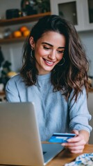 Fototapeta premium Young woman making online payment with credit card while using laptop in cozy kitchen