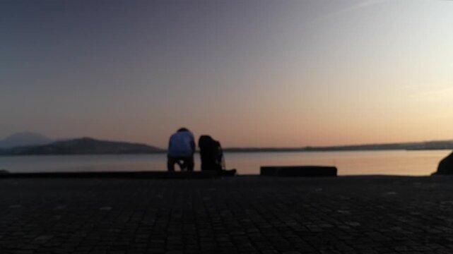 Silhouette of person sitting by Lake Zug Switzerland at sunset, peaceful leisure time atmosphere with calm water, alpine mountains and colorful evening sky in Switzerland
