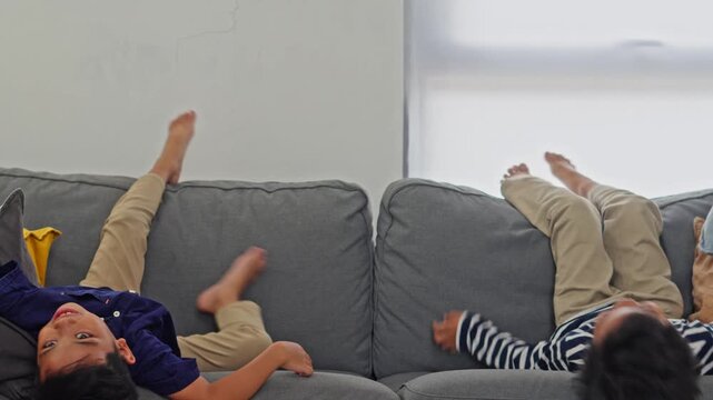Happy young boys in casual clothes hanging upside down on couch enjoying childhood fun