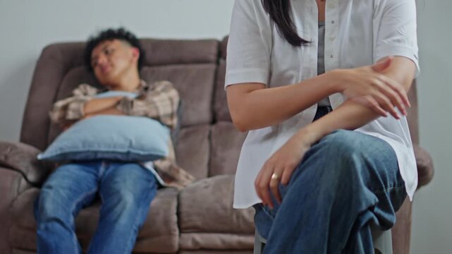 Upset wife fidgeting with wedding ring while her husband sits dejected in background