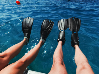 Two pairs of legs wearing black flippers dangling over deep blue sea water while sitting on boat deck during summer diving excursion © Dmitri