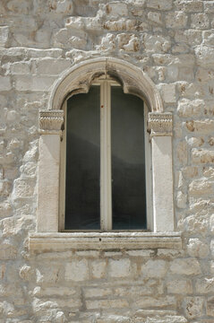 An elegant stone bifora window with a pointed arch and decorative capitals is set into a traditional limestone wall in Korcula