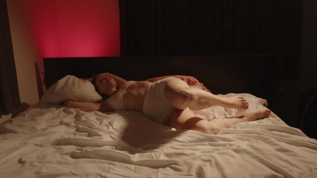 A beautiful woman wearing white panties and a bralette sensually poses in bed