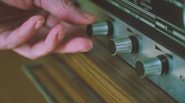 Close-up of hands operating multiple control dials on a 1970s German radiogram radio player. Useful for retro technology, audio equipment and broadcasting themes.