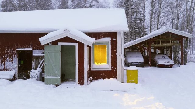 Drone pullback reveal of illuminated room in traditional Swedish house in winter