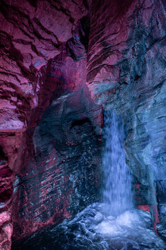 Cascate Varone small waterfall with purple and blue light inside rock cave with flowing water in parco grotta Trentino Italy