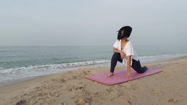 Woman practicing yoga stretching routine on sandy beach near ocean. Healthy lifestyle, wellness and mindfulness practice outdoors with calm peaceful sea background.