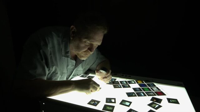 Male photo editor chooses among film slides on lightbox, copy space