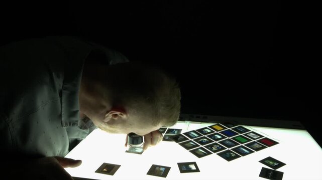 Male creative editor selects photo slides on lightbox in dark room