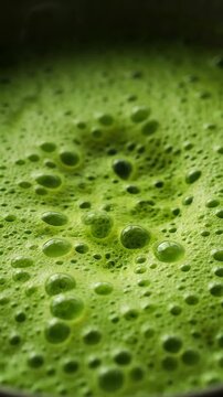 Frothy vibrant green pistachio latte drink with creamy texture and numerous bubbles. Vertical video.