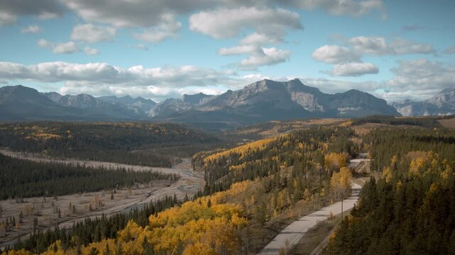 Booming up aerial shot mid-day autumn river bed and gravel road in the forest with mountain off in the distance.