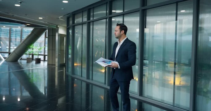 Desperate young executive reviewing printed documents and gestures expressively while holding documents in modern corporate office glass corridor - slow motion dolly in