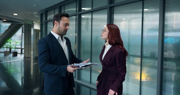 Furious businesswoman confronts male employee in corporate corridor, rejects his report, throws papers on floor, and walks away leaving him to pick them up - slow motion