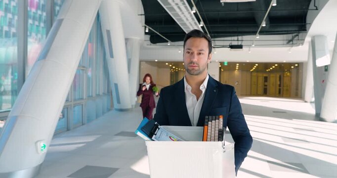 Two actors break character and laugh uncontrollably while filming layoff scene with businessman carrying belongings box in bright modern corridor
