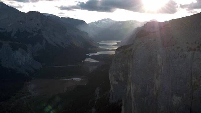 Aerial revealing a valley in the mountains with sun back lit during golden hour.