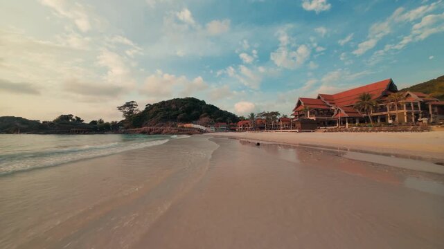 Fast cinematic FPV drone footage cruising low over the sandy coastal beach and ocean waves of Redang Island during a beautiful golden sunrise